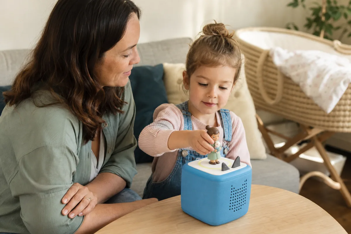Une enfant écoute une histoire sur l’arrivée d’un bébé avec sa mère et une Toniebox